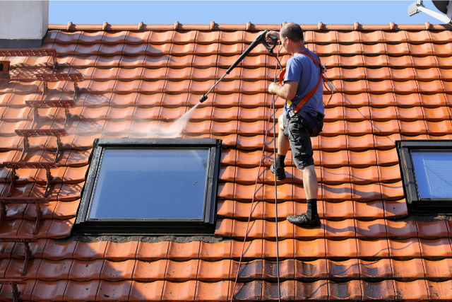 Roof cleaning with high pressure washer by worker